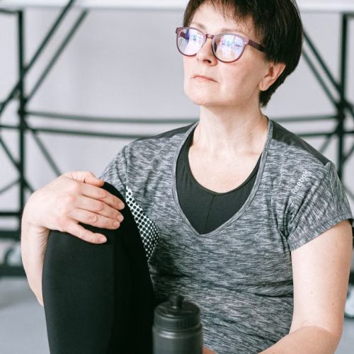 Senior woman resting during workout with water bottle indoors. Stay healthy and active.
