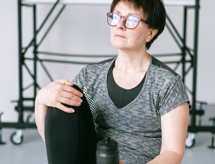 Senior woman resting during workout with water bottle indoors. Stay healthy and active.