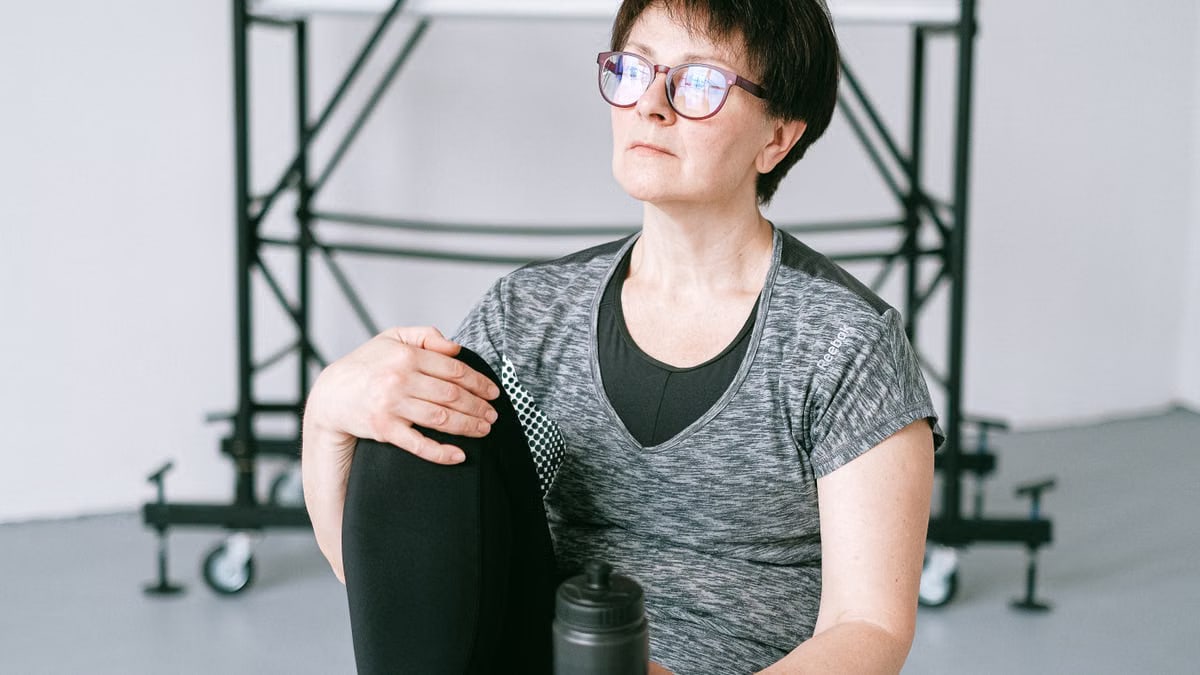 Senior woman resting during workout with water bottle indoors. Stay healthy and active.